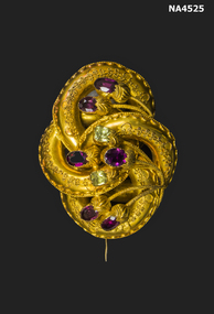 Curleche gold design with 6 purple and two green stones, can be worn as a brooch or used as a necklace or chain perhaps. The gold has been embossed. 
