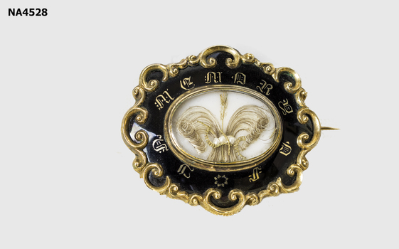 Gilt and black enamel oval brooch. Hair enclosed in centre with 'Prince of Wales' design and with tiny pearls. 