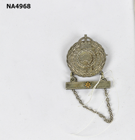 Silver-coloured Badge surmounted with crown edged with leaf design.