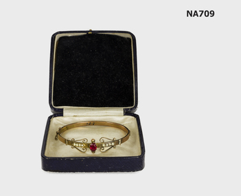 Gold bracelet with red stone and pearls in box.