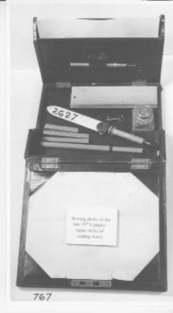 Black leather travelling writing case containing letter opener,(NA2627) six red sticks sealing wax, original glass and brass inkwell, and ruler. Case has compartments for paper blotting paper on lid. Workable lock (with key)and hinged lid.