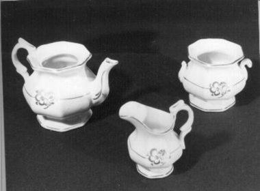 Cream china toy tea set with small gold pattern and edging. Comprises nine pieces - Two plates, cups and saucers, one milk jug, sugar pot with handles and tea pot