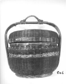 Cane sewing work basket with lid and stained dark red. It is actually a chinese basket(ie it has a loop on handle is for a pole when it was carried over the shoulder). Used by a lady's chair in the parlor.