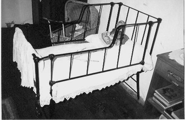 Black cast iron framed child's cot with higher sides at top. Cot folds up.