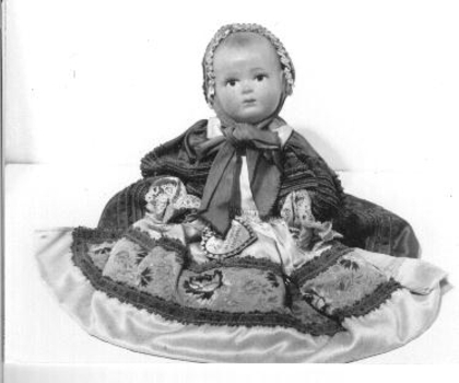 Celluloid doll in Breton France costume. Still has tag 'Le Minor Bretagne' on wrist. Dressed in purple satin dress with gold embroidered binding and white satin overskirt. Cap with red ribbon ties and long ribbons at back.
