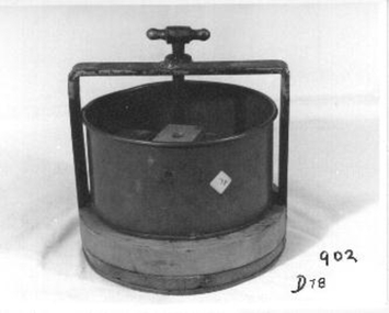 Round metal cheese press on wooden base. Metal frame with screw tap on top and wooden blocks inside to alter tension.