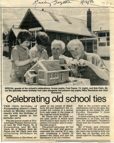 Article with image of two pupils and two older men sitting in front of school with cake in shape of school in front of them.