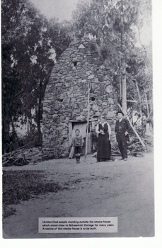  people standing outside the smoke house which stood close to Schwerkolt Cottage for many years. A replica of this smoke house has been built.