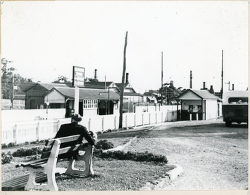 Black and white photo of Mitcham Railway Station 1945. In the foreground, man sitting on bench.
