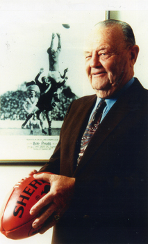 Bob Pratt holding a football with a photograph of him taking a mark in the background