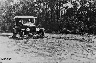 Large black and white photograph of Blackburn Road near Heath Street. A car driving through water with street behind