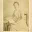 Amey Cook sitting on a chair with an open book on nearby table.