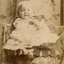 young dark haired child (2-3 years of age) sitting on a padded chair holding a basket. 