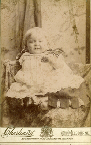 young dark haired child (2-3 years of age) sitting on a padded chair holding a basket. 