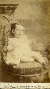 Amey Cook in a white dress sitting on a studio chair