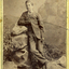 Young man wearing a dark suit leaning on a pile of studio rocks.  Inscriptions and Markings