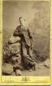 Young man wearing a dark suit leaning on a pile of studio rocks.  Inscriptions and Markings