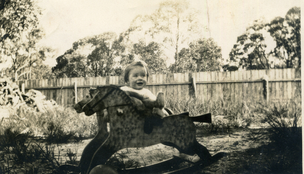 Female child and rocking horse in a garden with a wooden fence