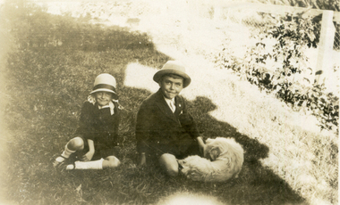 Two children sitting on a lawn with a dog.