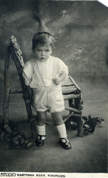 Studio photograph of Alwyn Till standing in front of a wooden chair.