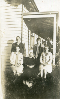 Family group on the verandah of a weatherboard house.