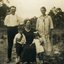 Three adults and two children in front of a wooden fence and trees.