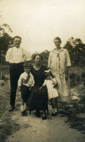 Three adults and two children in front of a wooden fence and trees.