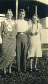 Family group: Evelyn, Alison and Alwyn Till standing in front of a weatherboard house.