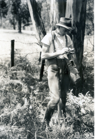 YEnglishoung man with a fishing rod, standing in front of a tree.