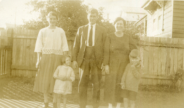 Till family group of three adults and two children standing in front of a wooden fence.