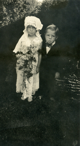 Two children Girl dressed in a white dress and hat, carrying a bouquet.  The boy wearing a suit and bow tie.