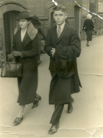Street scene of three people. Facing the camera, two people wearing winter clothes.