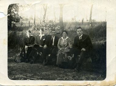 Five people sitting in a row in front of trees.