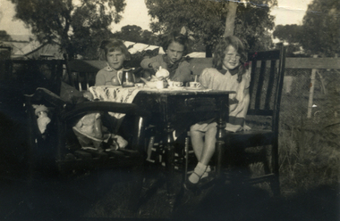 Three children sitting at a tea table.
