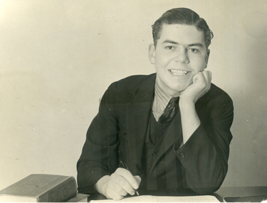 Alwyn Till sitting at a desk with pen in hand.