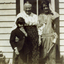 Two women & a female child standing outside a weatherboard building