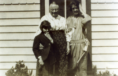 Two women & a female child standing outside a weatherboard building