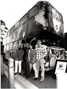 Photograph  of a decorated bus with four people standing in the centre of the photograph. 