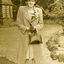 Alison Till wearing a hat and coat with corsage of flowers on lapel.