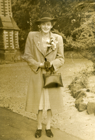 Alison Till wearing a hat and coat with corsage of flowers on lapel.
