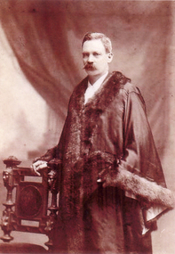 Mayoral robes with hand resting on ornamental chair.