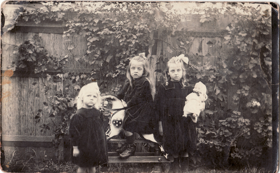 Three Lowen children outside in the garden, one on a hobby horse. 