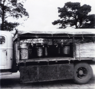 Black and white photograph of the side of a truck showing milk churns