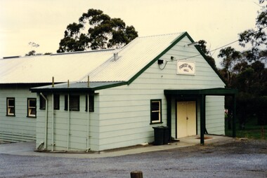 Coloured photograph of a green building with a yellow door. 