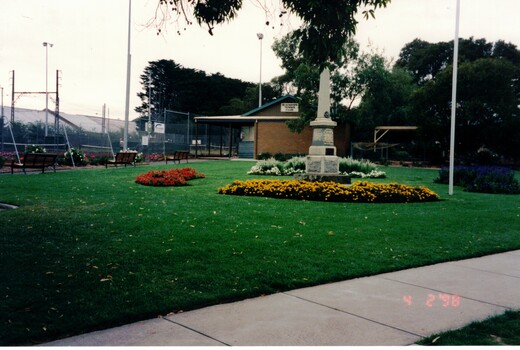 Photograph of a war memorial surrounded by flower gardens. 