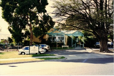 Photograph of a brick building with a blue canopy, cars parked in front and a council sign. 