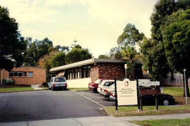 Coloured photograph of a brick building with cars parked nearby and a council sign at the front