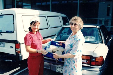 Coloured photograph of two women holding a container of prepared meals.