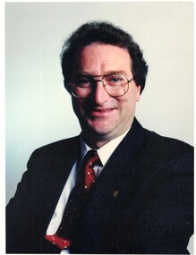  Peter Allan JP. Dark suit, Burgundy tie with yellow dots. Dark curly hair and wearing glasses