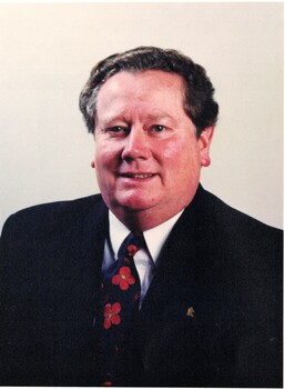 Coloured photograph of Kevin Abbott wearing a dark suit and tie with red flowers